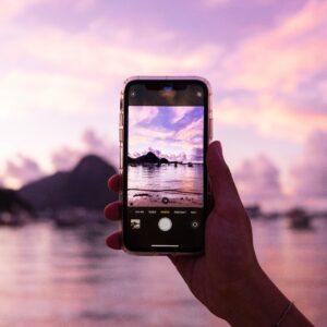 Backpacker tager billede med Iphone på stranden i pink solnedgang over vandet